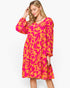 A woman modeling a long-sleeve V-neck midi dress with a vibrant pink and orange floral pattern, set against a plain white studio background.