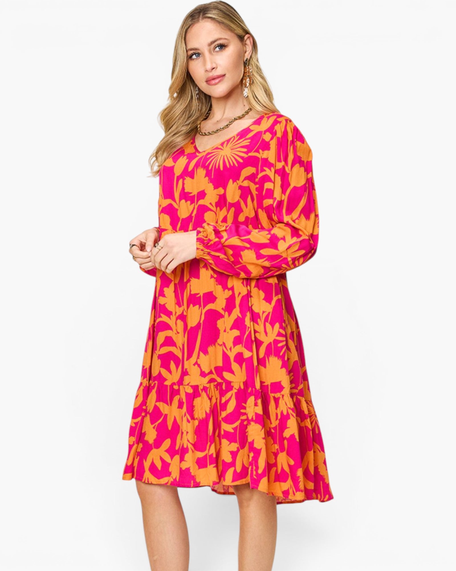 A woman modeling a long-sleeve knee-length dress with a bold abstract floral pattern in hot pink and orange against a clean white studio background.