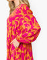 A close-up side view of a woman wearing a bright pink and orange floral print long-sleeve dress against a plain white background.