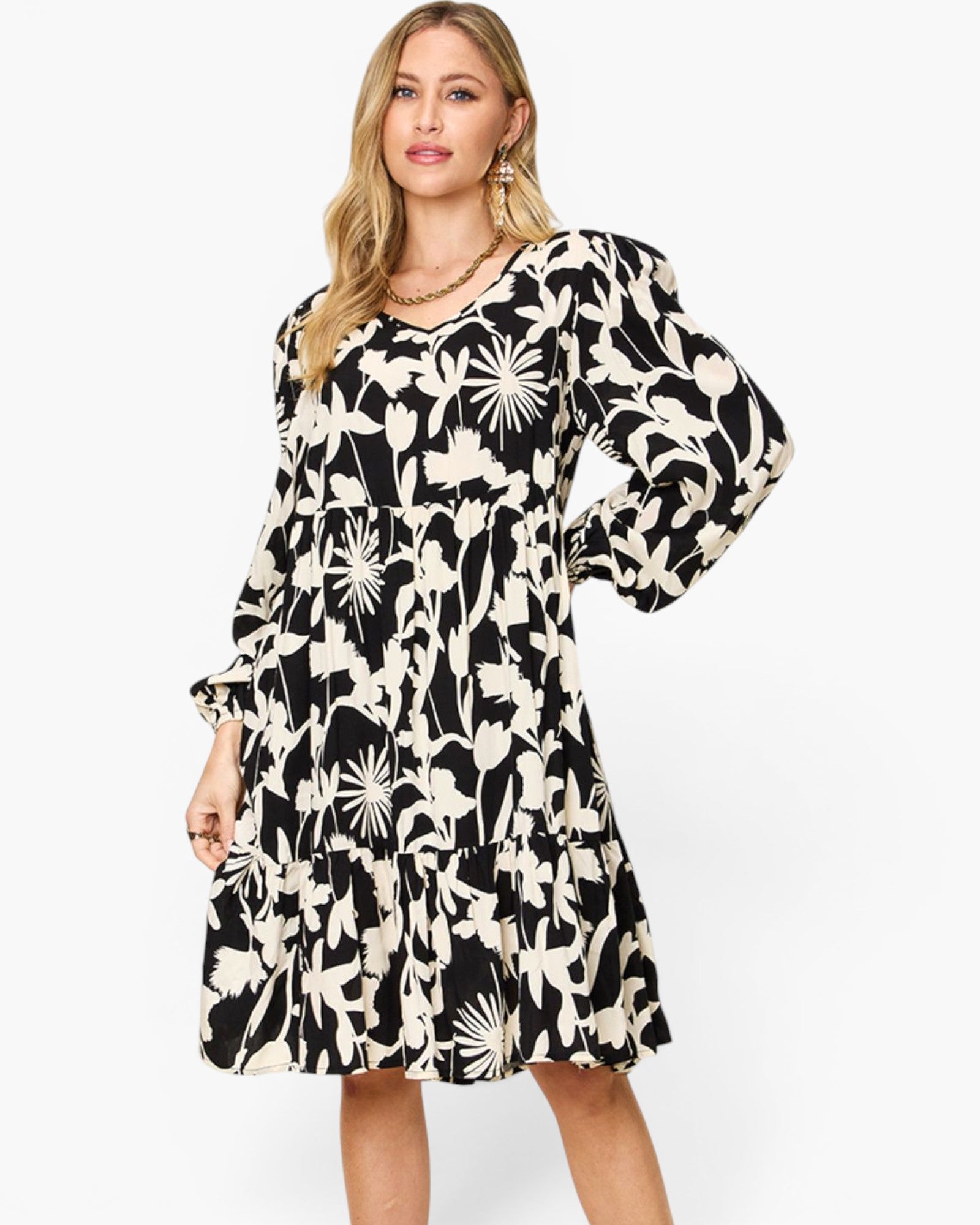 A woman modeling a black and cream floral print midi dress with long puff sleeves and a tiered skirt, set against a plain white studio background.