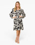 A woman modeling a knee-length black and cream floral print dress with long balloon sleeves, standing against a plain white studio background.