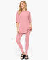 A woman modeling a matching dusty pink lounge set consisting of a short-sleeve tunic top and high-waisted leggings, paired with black slide sandals, against a plain white background.
