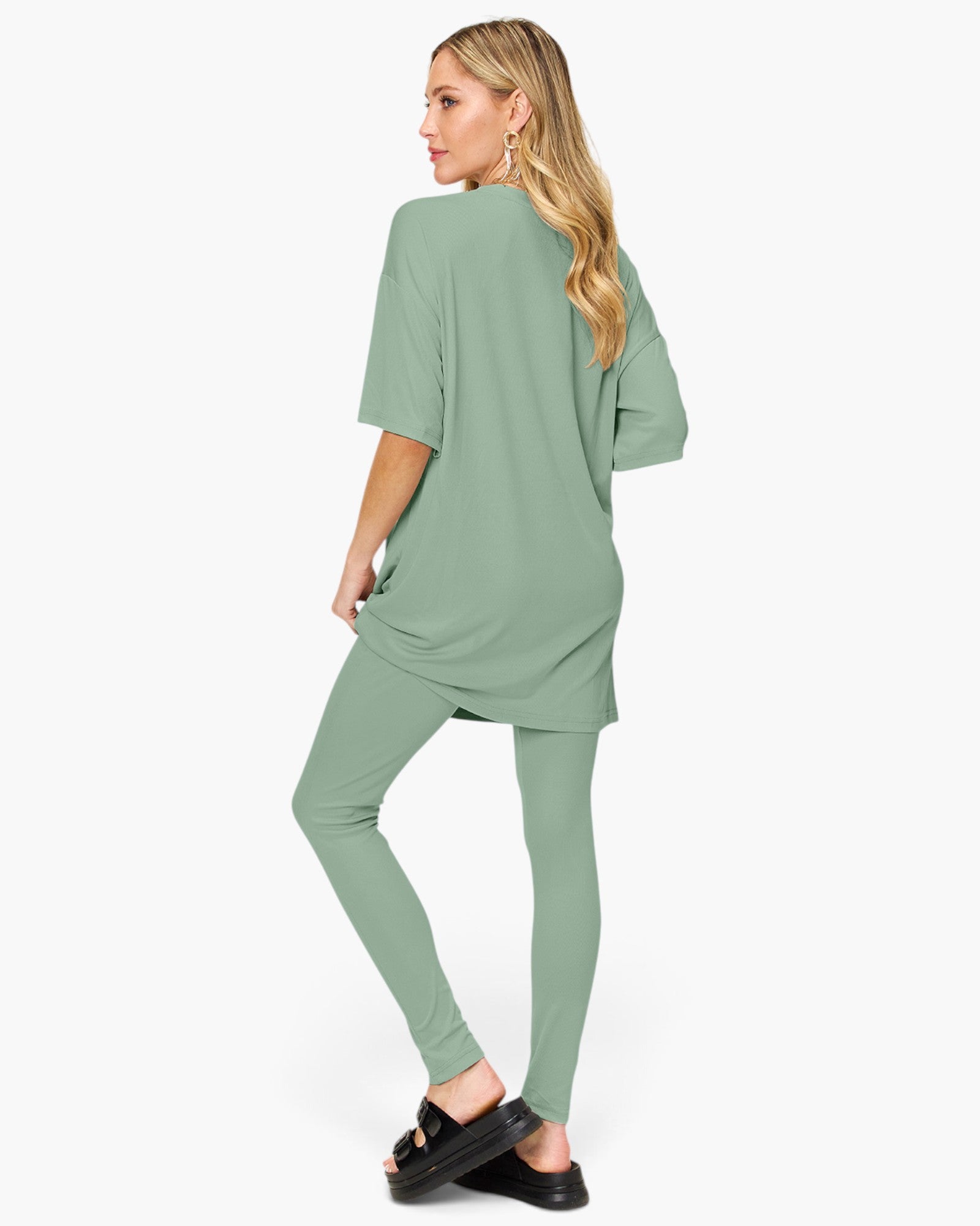 A woman modeling a sage green matching lounge set consisting of an oversized short-sleeve top and leggings, shown from a side-back angle against a plain white background.