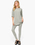 A woman modeling a light sage green two-piece lounge set consisting of a short-sleeve crewneck top and matching leggings, paired with black slide sandals, against a plain white studio background.