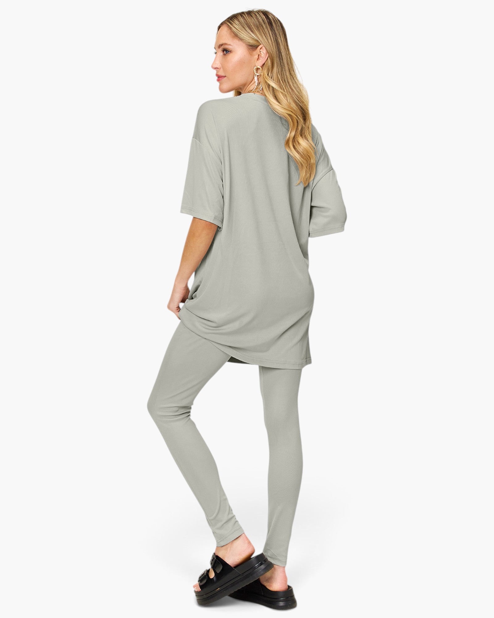 A woman modeling a light sage green two-piece lounge set consisting of an oversized short-sleeve top and matching leggings, shown from a side-back angle against a plain white studio background.