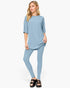 A woman modeling a light blue two-piece lounge set consisting of a short-sleeve top and matching leggings, paired with black slide sandals, against a plain white studio background.