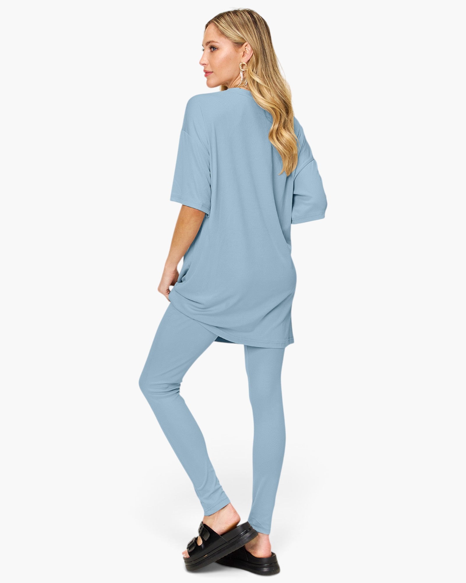 A woman modeling a light blue matching lounge set consisting of an oversized short-sleeve top and fitted leggings, shown from a side-back angle against a plain white studio background.
