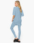 A woman modeling a light blue matching lounge set consisting of an oversized short-sleeve top and fitted leggings, shown from a side-back angle against a plain white studio background.