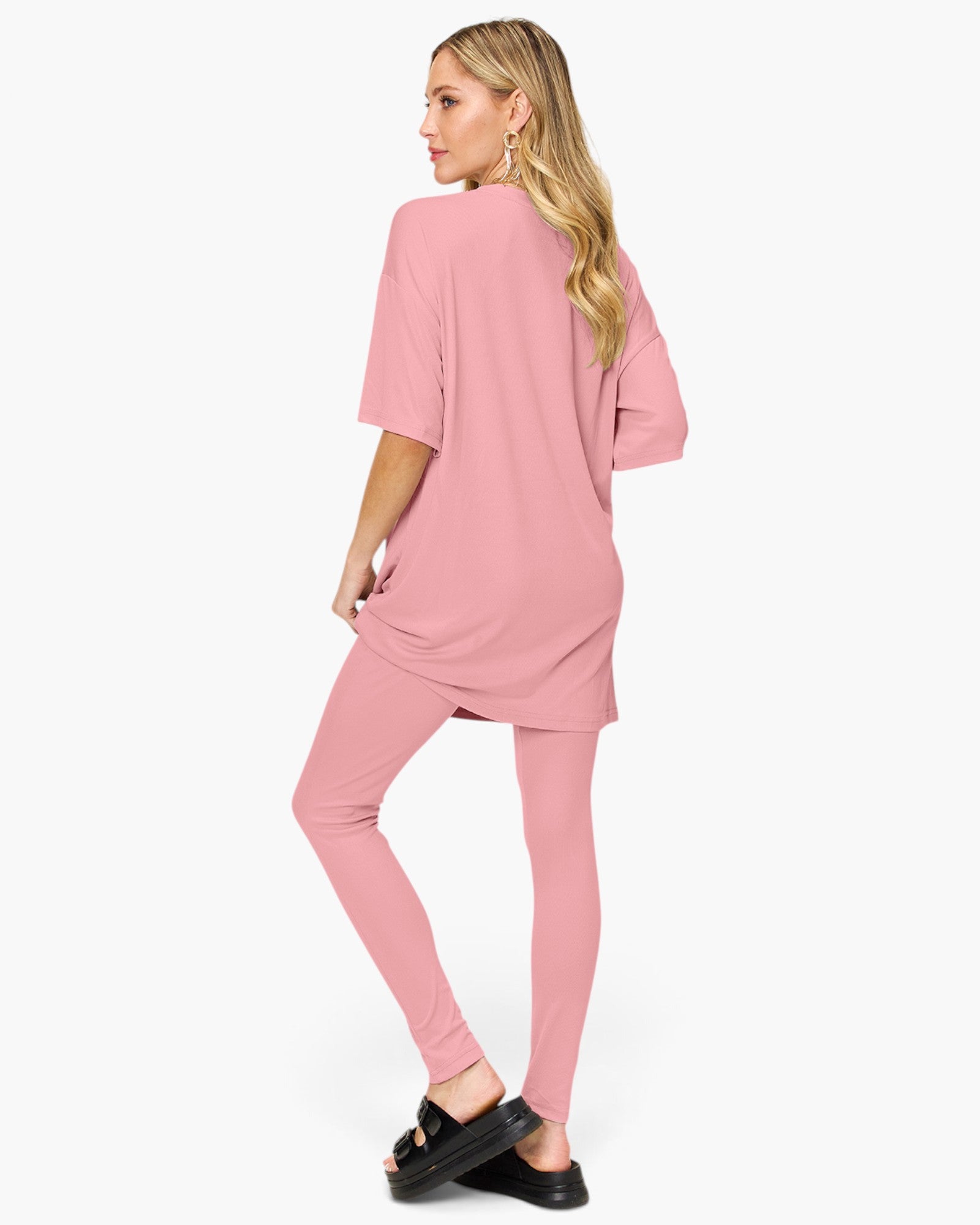 A woman modeling a matching dusty pink lounge set consisting of a short-sleeve tunic top and high-waisted leggings, shown from a three-quarters back view against a plain white background.