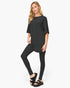 A woman modeling a black short-sleeve tunic top with matching black leggings and black platform sandals against a plain white studio background.