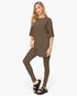 A woman modeling a matching two-piece lounge set consisting of an oversized short-sleeve top and high-waisted leggings in a solid taupe-brown color, paired with black platform sandals against a light gray background.
