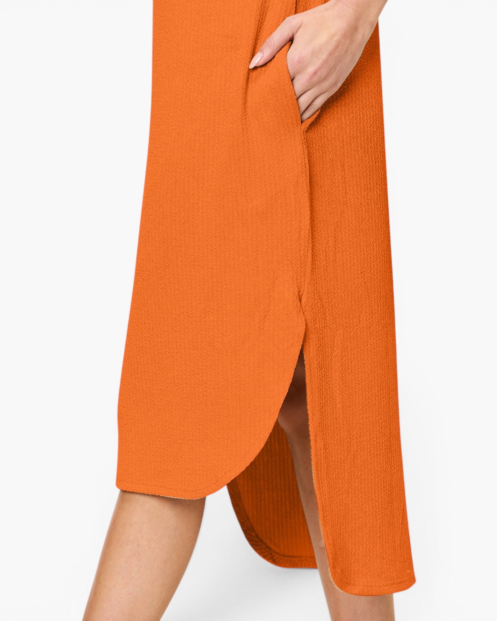 Close-up of a person wearing a bright orange ribbed midi dress with a side slit and hand tucked into the side pocket, against a plain light background.