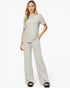 A woman modeling a light sage green two-piece lounge set consisting of a short-sleeve crewneck top and matching wide-leg pants, paired with black slide sandals against a plain white studio background.