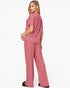 A woman modeling a dusty rose two-piece loungewear set consisting of a short-sleeve top and matching wide-leg pants, shown from a three-quarters back view against a plain white studio background.