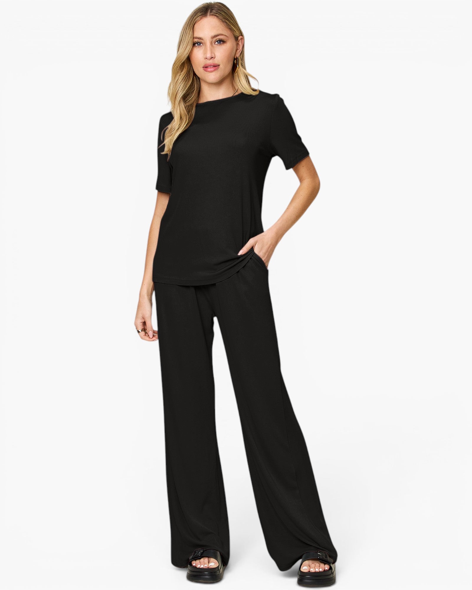 A woman modeling a black short-sleeve top and matching black wide-leg pants against a plain white studio background.