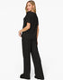 A woman modeling a black short-sleeve top and matching wide-leg pants, shown from a side-back angle against a plain white studio background.