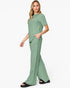 A woman modeling a sage green two-piece lounge set consisting of a short-sleeve crewneck top and matching wide-leg pants, paired with black slide sandals against a plain white background.