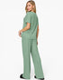 A woman modeling a sage green two-piece lounge set consisting of a short-sleeve top and matching wide-leg pants, shown from a three-quarters back angle against a plain white studio background.