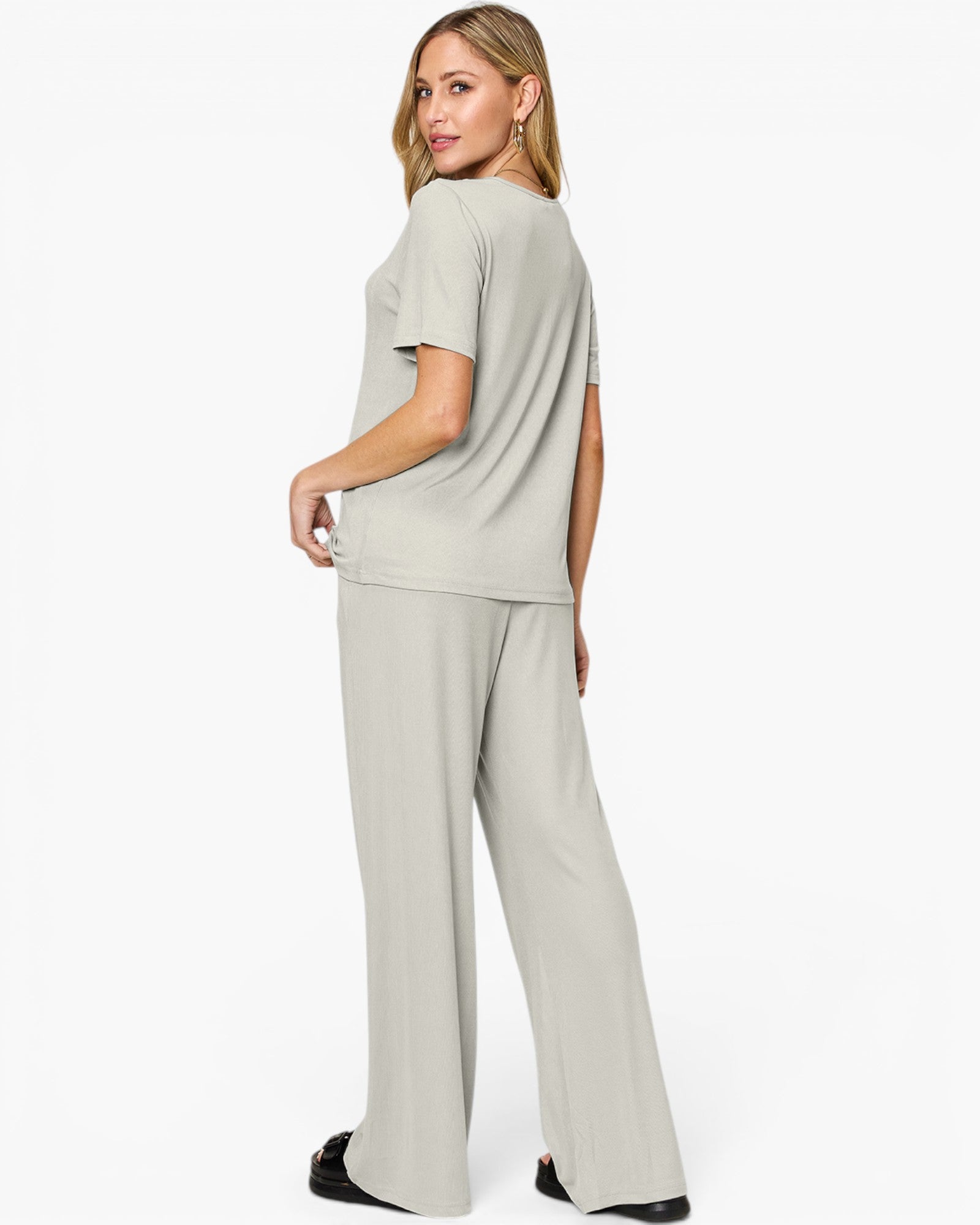 A woman modeling a light sage green two-piece loungewear set, consisting of a short-sleeve crewneck top and matching wide-leg pants, shown from a three-quarters back view against a plain white studio background.