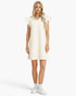 A woman modeling a cream-colored ribbed knit mini dress with ruffled cap sleeves and a ruffled collar, paired with white socks and white sneakers, against a plain white studio background.