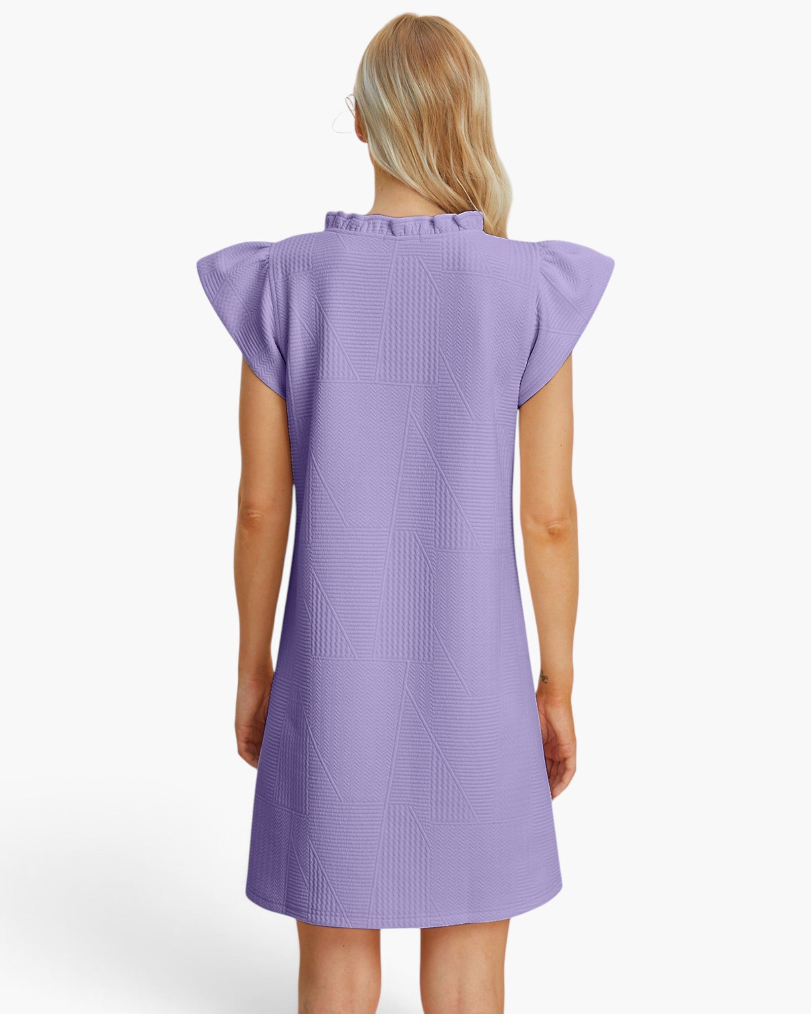 A woman viewed from the back wearing a lavender-purple textured dress with ruffled cap sleeves and a ruffled neckline, set against a plain white studio background.
