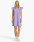 A woman modeling a light purple ribbed mini dress with ruffled cap sleeves and a ruffled collar, paired with white socks and white sneakers, against a light gray studio background.