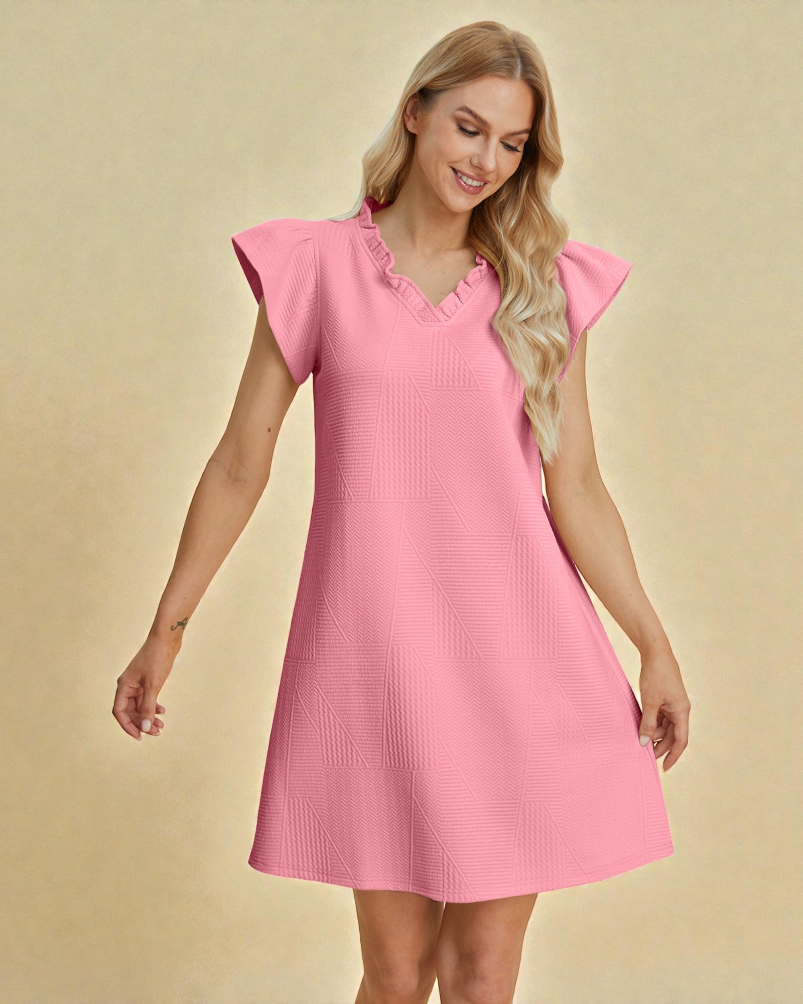 Woman wearing a pink dress with ruffled sleeves on a beige background