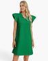 A woman modeling a bright green textured shift dress with ruffled cap sleeves and a split neckline, photographed against a clean white studio background.