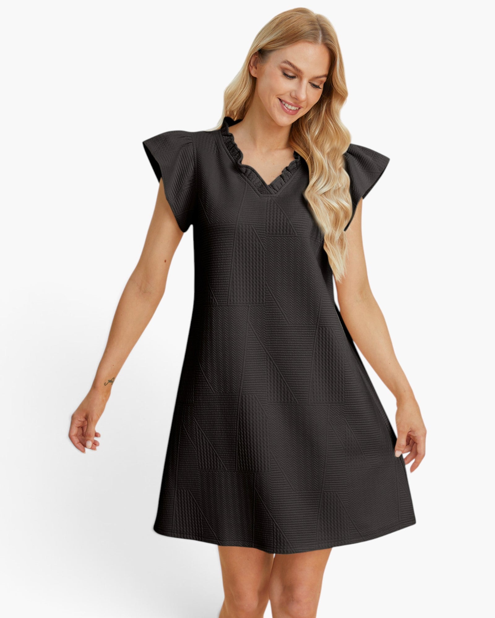 A woman modeling a black textured mini dress with flutter sleeves and a ruffled V-neckline, photographed against a clean white studio background.