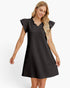A woman modeling a black textured mini dress with flutter sleeves and a ruffled V-neckline, photographed against a clean white studio background.