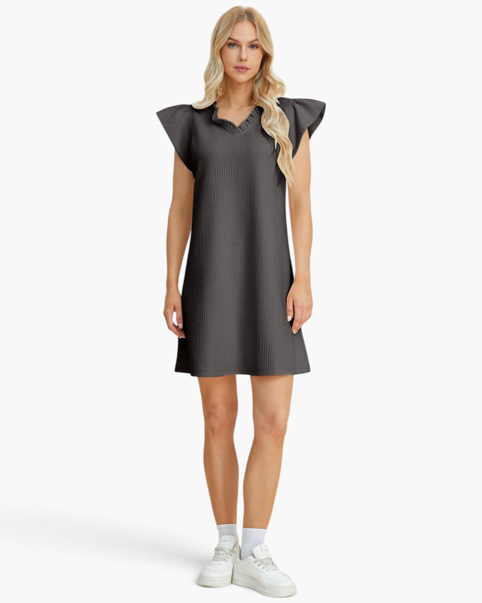 A woman modeling a dark gray ribbed mini dress with ruffled shoulder details, paired with white socks and white sneakers, against a light gray studio background.