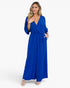 A woman modeling a royal blue maxi jumpsuit with a wrap-style V-neck, elbow-length sleeves, side pockets, and a tie waist, photographed against a clean white studio background.