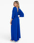 A woman modeling a royal blue maxi dress from the back, featuring a deep V-neckline with tie details, wide three-quarter sleeves, and a gathered waist, set against a plain white studio background.
