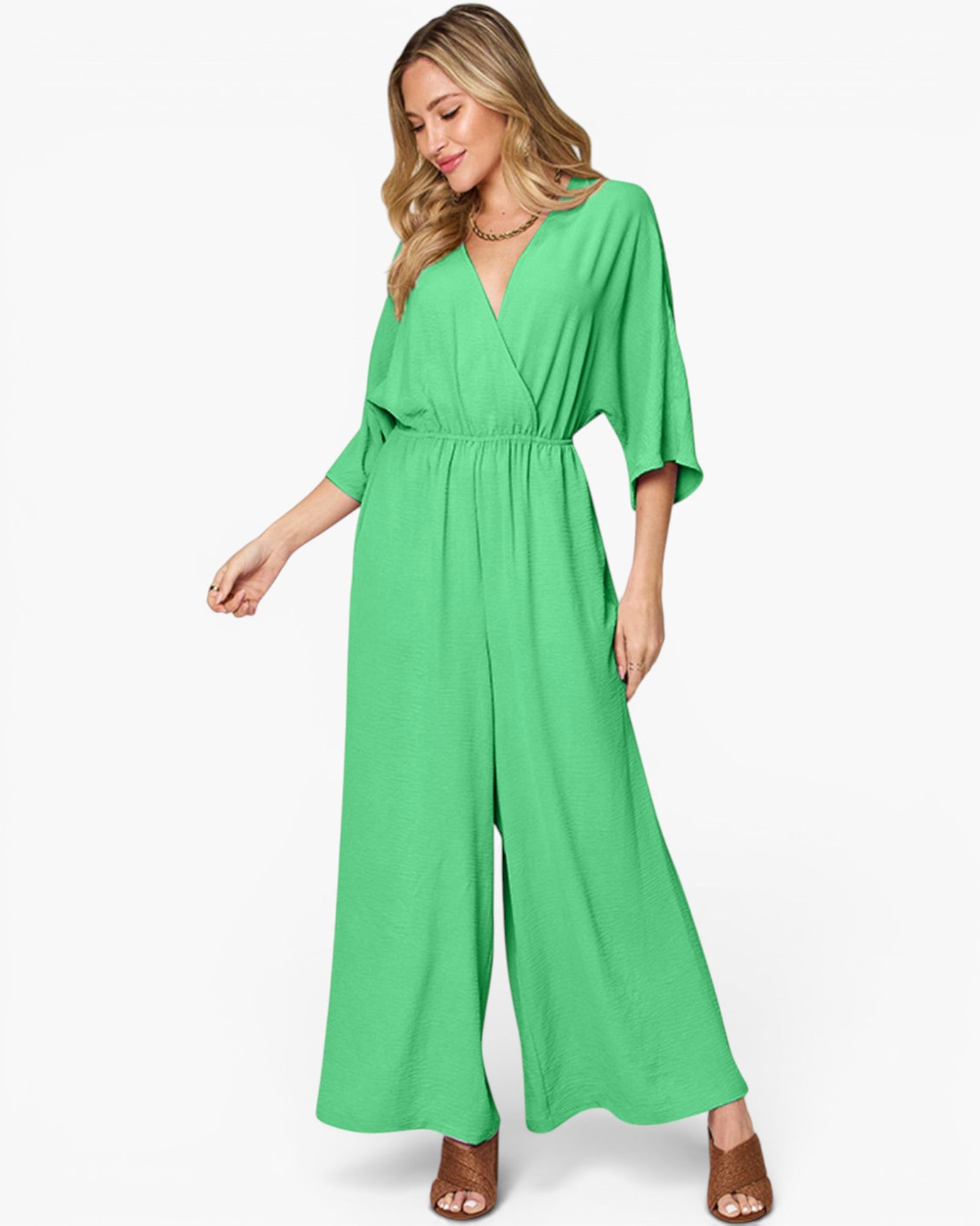 A woman modeling a bright green wide-leg jumpsuit with a wrap-style V-neck bodice and elbow-length sleeves, photographed against a clean white studio background.