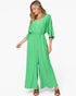 A woman modeling a bright green wide-leg jumpsuit with a wrap-style V-neck bodice and elbow-length sleeves, photographed against a clean white studio background.