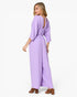 A woman modeling a lavender purple jumpsuit with three-quarter sleeves, a wrap-style waist, and an open back, shown against a plain white studio background.