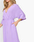 A woman wearing a light purple wrap-style midi dress with wide three-quarter sleeves and side pockets, shown against a plain white background.