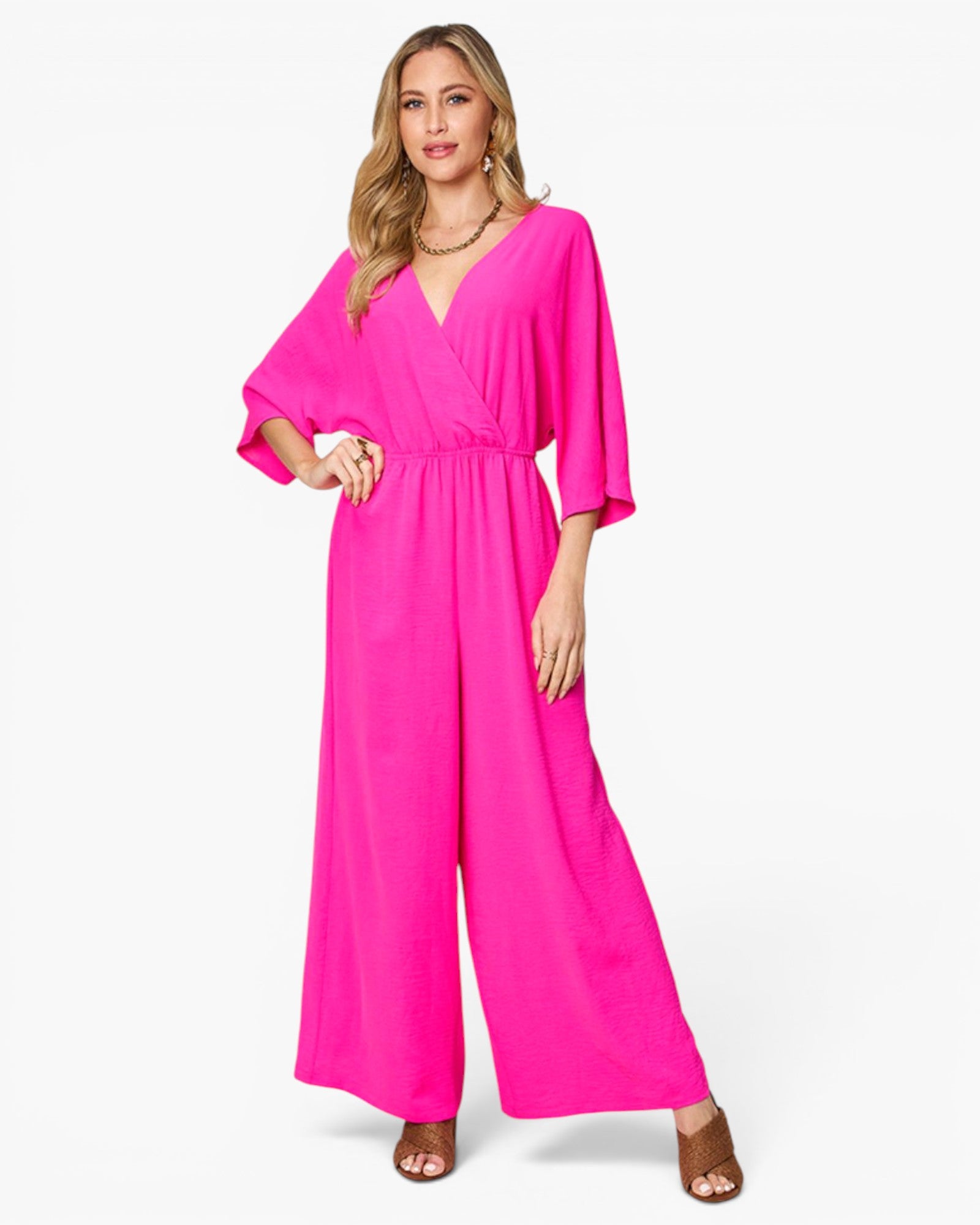 A woman modeling a bright hot pink wide-leg jumpsuit with a wrap-style V-neck bodice and elbow-length sleeves, photographed against a clean white studio background.