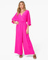 A woman modeling a bright hot pink wide-leg jumpsuit with a wrap-style V-neck bodice and elbow-length sleeves, photographed against a clean white studio background.