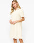 A woman modeling a short-sleeve collared shift dress in a warm off-white or cream color, photographed against a clean white studio background.