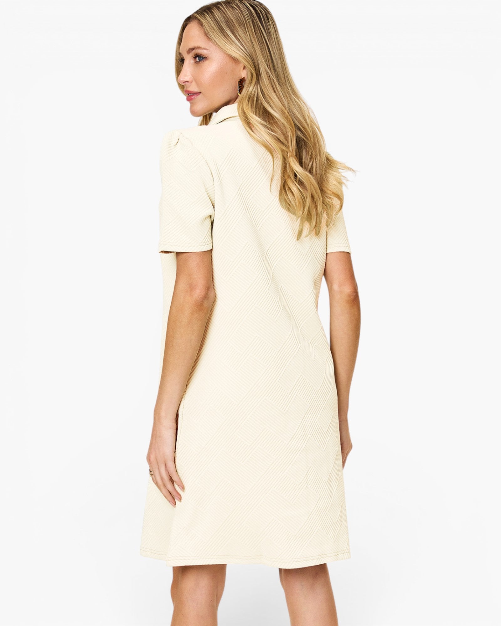 A woman with blonde hair is shown from the back wearing a short-sleeve cream-colored dress against a plain white background.
