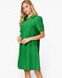 A woman modeling a bright green short-sleeve collared dress with a subtle textured pattern, set against a plain white studio background.