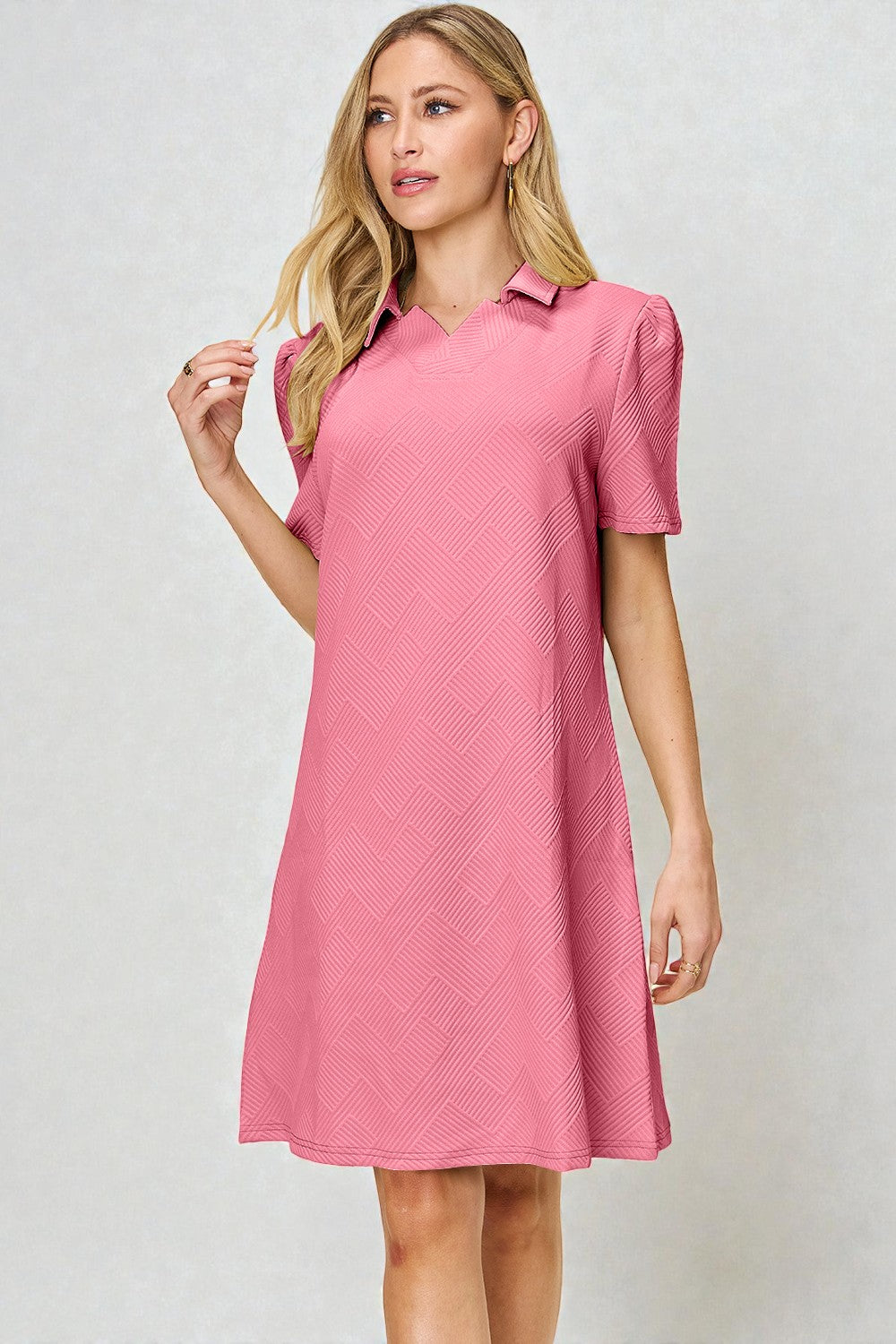 Woman wearing a pink dress with a collar against a light gray background