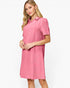 A woman modeling a pink short-sleeve collared dress with a subtle textured pattern, set against a plain light gray studio background.