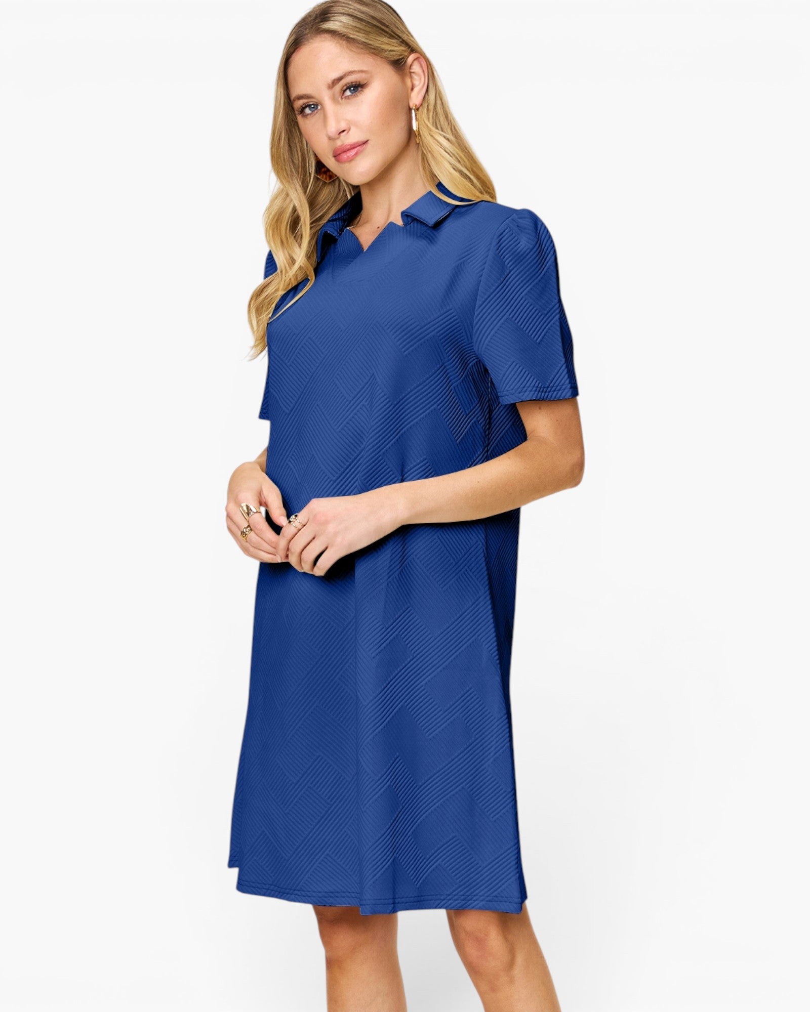 A woman modeling a short-sleeve collared shift dress in a medium royal blue color with a subtle textured pattern, set against a plain white studio background.