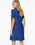 A woman modeling a royal blue short-sleeve dress from the back, featuring a textured geometric pattern and a high mock neck, against a plain white studio background.