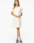 A woman modeling a short-sleeve collared shift dress in off-white, paired with blue slide sandals, against a plain white studio background.