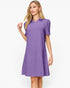 A woman modeling a short-sleeve purple polo dress with a subtle textured pattern, set against a plain white studio background.
