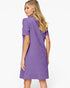 A woman modeling a short-sleeve purple dress from the back, featuring a textured geometric pattern and a high mock neck, against a plain white background.