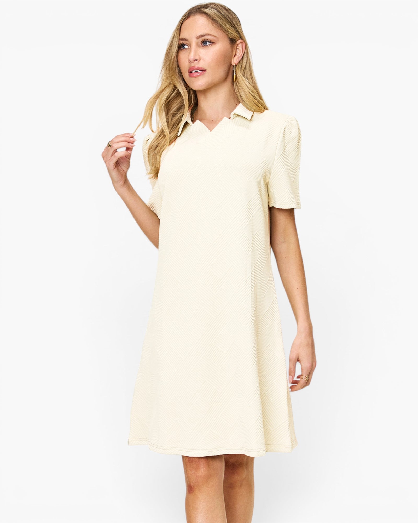 A woman modeling a short-sleeve polo dress in a light cream or off-white color, set against a plain white studio background.